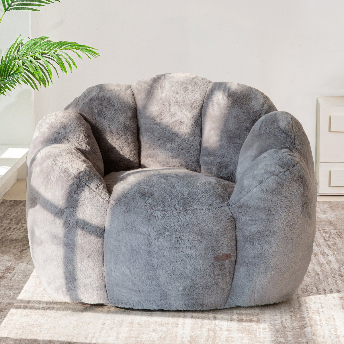 A dark grey, floral shaped bean bag chair made of ultra soft faux fur, positioned in a well-lit room with a shadow falling over part of the floor.